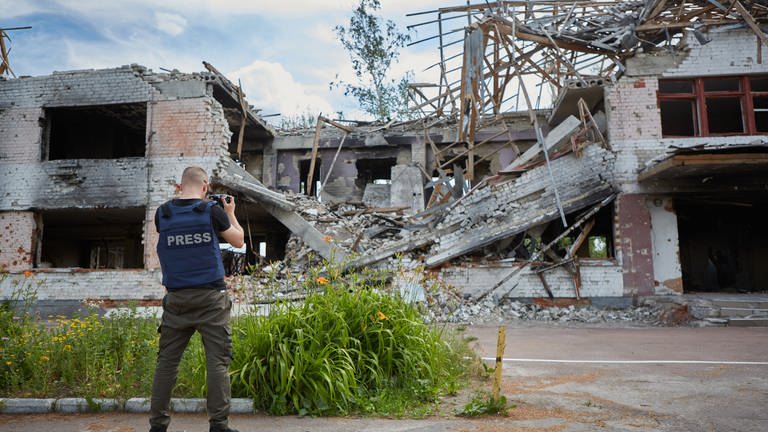 Ein Fotoreporter mit der Veste "Press" fotografiert bombardierte Gebäude (Foto: IMAGO, IMAGO / Pond5 Images)